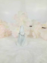 Charger l'image dans la galerie, La Bague Nourri-Source, une délicate bague en argent au design cœur ouvert de MONA fine joaillerie, est exposée sur un socle en marbre de forme conique. Le fond est doux et flou avec des fleurs rose pastel et blanches, créant une atmosphère douce et romantique qui capture parfaitement l'essence du style minimaliste.