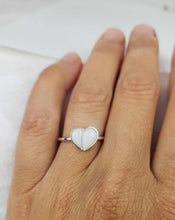 Charger l'image dans la galerie, Gros plan d'une main portant la Bague Nourri-Source de MONA fine joaillerie à l'annulaire. Le cœur, rempli de matière blanche et lisse, dégage une élégance raffinée typique du savoir-faire de MONA. Le style minimaliste est accentué par l'anneau mince. Le flou d’arrière-plan concentre toute l’attention sur le charme de la bague.