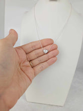 Charger l'image dans la galerie, Une main tenant une chaîne en argent Collier Nourri-Source de 10 mm avec un petit pendentif en forme de cœur, présentée sur un buste de bijoux blanc sur fond neutre. Le pendentif, pièce exquise de MONA joaillerie fine, est tenu délicatement entre le pouce et l'index.