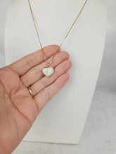 Charger l'image dans la galerie, Une main tenant le Pendentif Nourri-Source 12 mm MONA fine joaillerie, un collier en or avec un pendentif en forme de cœur orné d'une incrustation nacrée blanche. Le savoir-faire élégant du collier et du pendentif en or 10 carats est évident, probablement affiché sur un support de collier sur un fond blanc.