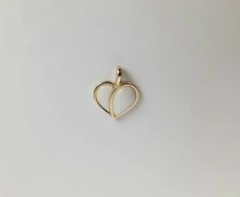 Charger l'image dans la galerie, Un délicat pendentif en or, nommé Pendentif Nourri-Source 12 mm et fabriqué en or 10 carats par MONA fine joaillerie, présente deux cœurs superposés avec des espaces ouverts minimalistes à l'intérieur de leurs contours, sur un fond blanc uni.