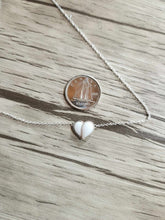Charger l'image dans la galerie, Un délicat Collier Nourri-Source 10 mm de MONA joaillerie fine avec un petit pendentif blanc en forme de cœur est exposé à côté d'une pièce de 10 cents canadienne, soulignant la taille du pendentif. Le collier et la pièce sur mesure sont placés sur une surface en bois.