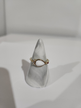 Charger l'image dans la galerie, Une élégante bague Bague London avec une pierre précieuse ovale centrale flanquée de petits diamants d'accent, présentée sur un présentoir blanc dans le cadre de notre collection de bijoux personnalisés de MONA fine joaillerie.