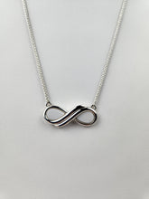 Charger l'image dans la galerie, Un pendentif Collier Infinity en argent de MONA joaillerie fine sur une chaîne délicate repose sur un fond blanc, symbolisant l'éternité et l'amour éternel. Cette pièce offre une option d'inclusions personnelles.