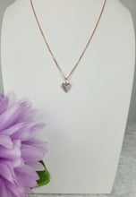 Charger l'image dans la galerie, Pendentif Mini Coeur de MONA fine joaillerie : collier en or rose avec un petit pendentif cœur, présenté sur un socle blanc avec une fleur violette en bas à gauche.