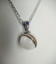 Charger l'image dans la galerie, Un gros plan d'un élégant pendentif MONA fine joaillerie Pendentif Double Zircon comportant une pierre précieuse blanche ronde à bandes avec un accent de saphir, suspendue à une chaîne en argent sur un fond doux.