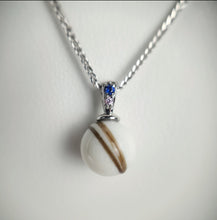 Charger l'image dans la galerie, Un délicat Pendentif Double Zircon de MONA fine joaillerie comportant une perle aux stries brunes uniques suspendue à une chaîne en argent, accentuée par une petite pierre précieuse bleue étincelante au niveau de la bélière.
