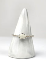 Charger l'image dans la galerie, La Bague Goutte de vie (avec zircons) de MONA fine joaillerie est une bague en argent ornée d'une pierre blanche en forme de goutte et d'un fin anneau serti de zircons étincelants, présentée sur un support conique en marbre blanc sur un fond doux.