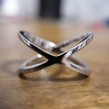 Charger l'image dans la galerie, Gros plan d'une Bague Crossover élégante et brillante de MONA fine joaillerie avec un design en forme de X, placée bien en évidence sur une surface en bois floue.