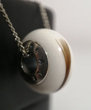 Charger l'image dans la galerie, Photographie en gros plan d'un pendentif Perle européenne de Bijoux La Précieuse avec un design rond, blanc, semblable à une pierre, comportant une inclusion et suspendu à une chaîne en argent, mettant en valeur un petit croissant de lune et une étoile en métal incrustés sur sa surface.