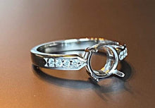 Charger l'image dans la galerie, Une bague Bague Précieuse de 8 mm de MONA fine joaillerie avec une pierre précieuse centrale manquante, comportant de petits zircons sur son anneau, repose sur une surface réfléchissante avec un fond soft focus.