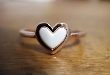 Charger l'image dans la galerie, Un gros plan d'une bague Bague Coeur avec une incrustation blanche sur une surface en bois, exprimant un symbole d'amour subtil mais élégant par MONA fine joaillerie.