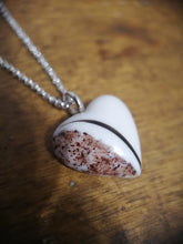 Charger l'image dans la galerie, Un Pendentif Oeillet en forme de cœur de MONA fine joaillerie avec une combinaison unique de textures blanches et marron mouchetées, avec une élégante inclusion de lait maternel, suspendu à une chaîne en argent, reposant sur une surface en bois.