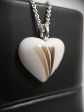 Charger l'image dans la galerie, Gros plan d'un pendentif Oeillet en forme de cœur avec un motif marron et blanc unique, représentant l'inclusion de lait maternel, suspendu à une chaîne en argent et affiché sur un fond sombre. Cette pièce est MONA fine joaillerie.