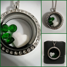 Charger l'image dans la galerie, Un collage d'un Médaillon Pendentif en acier inoxydable Bijoux La Précieuse avec des cristaux décoratifs et des pierres précieuses vertes entourant un cœur blanc central, affiché sur un fond blanc et présenté sur un support noir dans l'une des images.