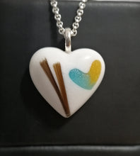 Charger l'image dans la galerie, Un Pendentif Oeillet avec un art coloré et une mèche de cheveux enfermée à l'intérieur, suspendue sur un fond noir. Cette pièce est de MONA fine joaillerie, mettant en valeur leur savoir-faire en bijoux sur