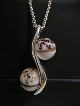 Charger l'image dans la galerie, Un élégant pendentif avec deux pierres mouchetées enchâssées dans une monture argentée tourbillonnante, rappelant un symbole de l'infini, affiché sur un fond sombre. Cette pièce est un bel exemple du Pendentif double perle "S" de MONA fine joaillerie.