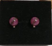 Charger l'image dans la galerie, Une paire de Boucles d'oreilles Juri sphériques violettes avec un détail de rayures argentées sur fond noir.