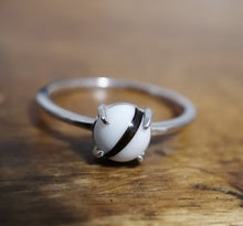 Charger l'image dans la galerie, Un gros plan d'une Bague Unique de joaillerie fine MONA avec une seule perle blanche de 6 mm sertie dans un serti griffe minimaliste, sur un fond en bois.