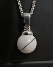Charger l'image dans la galerie, Un Pendentif Bélière Clara sphérique blanc simple et élégant avec un design de ligne diagonale singulière, suspendu à une chaîne en argent, présenté sur un fond sombre à la Bijouterie Langlois.