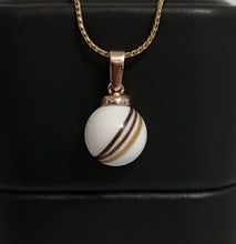 Charger l'image dans la galerie, Un Pendentif Bélière Clara de la Bijouterie Langlois comportant une pierre ronde rayée blanche et brune avec inclusions, sertie dans une monture dorée, exposée sur un fond noir.