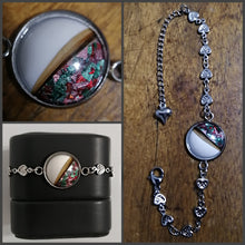 Charger l'image dans la galerie, Un collage de trois photographies présentant un bracelet chaîne en coeur Bijoux La Précieuse avec une breloque dotée d'un pendentif rond rempli de taches colorées sur une surface en bois et rangé dans une boîte noire.