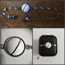Charger l'image dans la galerie, Un collage de trois images présentant un bracelet chaîne en coeur de Bijoux La Précieuse, avec un pendentif rond blanc comportant une seule bande marron, complété par des motifs de maillons complexes et une petite breloque, présentés tous deux librement.