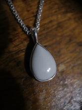 Charger l'image dans la galerie, Un pendentif Goutte15 contenant du lait maternel sur une chaîne en argent, reposant sur une surface en bois, sa surface lisse brillant subtilement sous la lumière par MONA fine joaillerie.