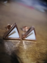Charger l'image dans la galerie, Une paire de Boucles d'oreilles triangulaires en or rose avec une incrustation blanche, élégamment positionnées sur une surface en bois avec un fond flou soulignant leurs détails, mettant en valeur le savoir-faire de la fine joaillerie MONA.