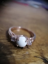 Charger l'image dans la galerie, Gros plan d'une élégante Bague Trinité de la Bijouterie Langlois, flanquée de deux pierres précieuses étincelantes, serties sur une surface en bois aux tons chauds.