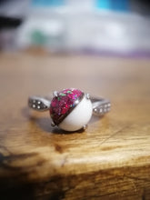 Charger l'image dans la galerie, Gros plan d'une bague Bague modèle 3 de Bijoux La Précieuse avec une demi-perle mouchetée de rose et de blanc sertie entre des montures à griffes, reposant sur une surface en bois.