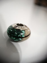 Charger l'image dans la galerie, Un gros plan d'une Perle européenne Luxe ronde et brillante de MONA fine joaillerie avec un design vert chatoyant et beige sable, baignée d'un éclairage doux sur une surface réfléchissante.