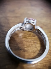 Charger l'image dans la galerie, Un gros plan d'une bague de fiançailles solitaire Bague Précieuse de 8 mm avec demi-perle et zircons, placée sur une surface en bois, mettant en valeur les détails complexes et l'anneau brillant en or 10 carats de MONA fine joaillerie.