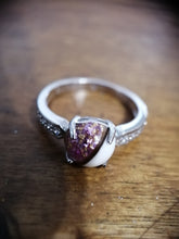 Charger l'image dans la galerie, Une élégante Bague Précieuse 8 mm de MONA fine joaillerie avec une pièce maîtresse en pierres précieuses violettes et des zircons plus petits sertis sur une surface en bois.
