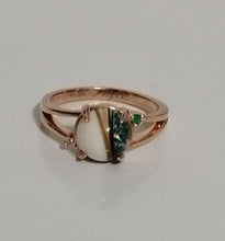 Charger l'image dans la galerie, Bague Angélique en or rose avec une pierre blanche centrale entourée de petites pierres précieuses vertes sur une surface réfléchissante.