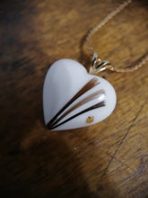 Charger l'image dans la galerie, Un pendentif en forme de cœur avec un motif de plume complexe reposant sur une surface en bois est un pendentif RG130 de Bijoux La Précieuse.