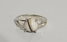Charger l'image dans la galerie, Une bague Bague Angélique avec une pièce maîtresse en pierre blanche flanquée de petits diamants sur une surface réfléchissante, de MONA fine joaillerie.