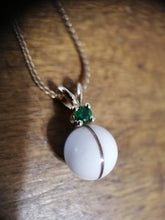 Charger l'image dans la galerie, Un élégant Pendentif Juri de la Bijouterie Langlois comportant une pierre sphérique blanche lisse avec une bande centrale, accentuée par une petite pierre précieuse verte riche sur une délicate chaîne en argent sterling 925.