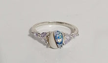 Charger l'image dans la galerie, Une élégante bague Bague Brielle en or 10 carats avec une pierre précieuse bleue centrale flanquée de motifs complexes, probablement des cristaux ou des diamants, sur une surface blanche par MONA fine joaillerie.