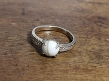 Charger l'image dans la galerie, Une élégante Bague Précieuse de 8 mm en ou 10 carats avec une pierre précieuse blanche, présentant de délicates gravures sur l'anneau, reposant sur une surface en bois. Fabriqué par MONA fine joaillerie.