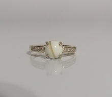 Charger l'image dans la galerie, Une élégante Bague Précieuse 8 mm de MONA fine joaillerie comportant une pierre précieuse ovale centrale flanquée d'une bande rehaussée de petits zircons étincelants, présentée sur un fond blanc épuré.