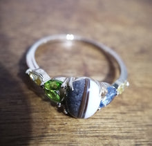 Charger l'image dans la galerie, Gros plan d'une Bague Brielle de MONA fine joaillerie ornée d'une pierre centrale aux motifs rayés, flanquée de petites pierres précieuses vertes.
