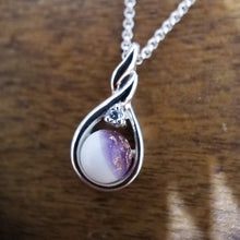 Charger l'image dans la galerie, Un élégant Pendentif Amiko de Bijouterie Langlois avec une pierre précieuse violette et blanche, accentuée par un petit zircon de couleur diamant, suspendu à une chaîne en argent sur une surface en bois.