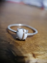 Charger l'image dans la galerie, Une élégante Bague Unique de MONA fine joaillerie avec une seule perle de 6 mm sertie entre quatre griffes, présentée sur une surface en bois avec un fond flou.