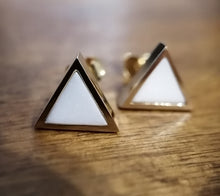 Charger l'image dans la galerie, Une paire de boucles d'oreilles triangulaires en fine joaillerie MONA avec une incrustation centrale de lait maternel, reposant sur une surface en bois.