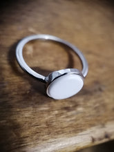 Charger l'image dans la galerie, Une Bague Coupe fine de MONA fine joaillerie avec une pierre blanche ovale, reposant sur une surface en bois.