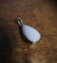 Charger l'image dans la galerie, Gros plan d'un pendentif Goutte15 en argent à surface lisse, réalisé par MONA fine joaillerie, reposant sur un fond en bois.