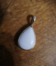 Charger l'image dans la galerie, Un pendentif Goutte15 blanc en forme de larme, confectionné avec du lait maternel, dans une monture en argent sur une surface en bois par MONA fine joaillerie.