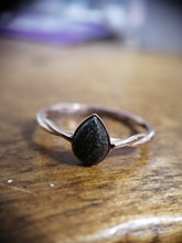 Charger l'image dans la galerie, Un gros plan d'une élégante Bague Twist avec une pierre noire sertie dans un anneau torsadé en or rose, reposant sur une surface en bois par MONA fine joaillerie.