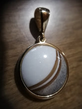 Charger l'image dans la galerie, Un élégant pendentif Cabella de MONA fine joaillerie avec une incrustation circulaire de pierres précieuses présentant des tons superposés de blanc et de gris, capturés sur une surface en bois sous un éclairage chaleureux.